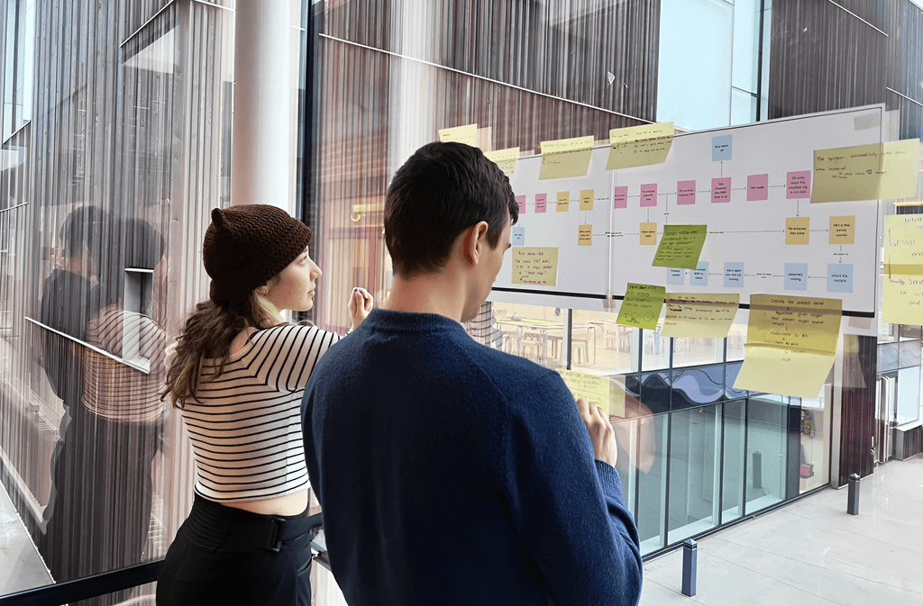 Team members arranging research notes and interface ideas on a workshop wall.