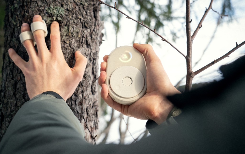 A person touches tree bark with finger-mounted sensors while holding a Chime recorder.