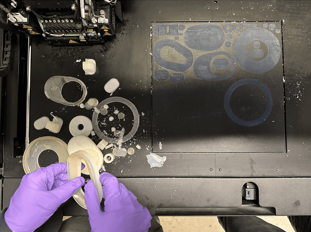 Hands assembling circular recorder components beside a laser-cutting bed.