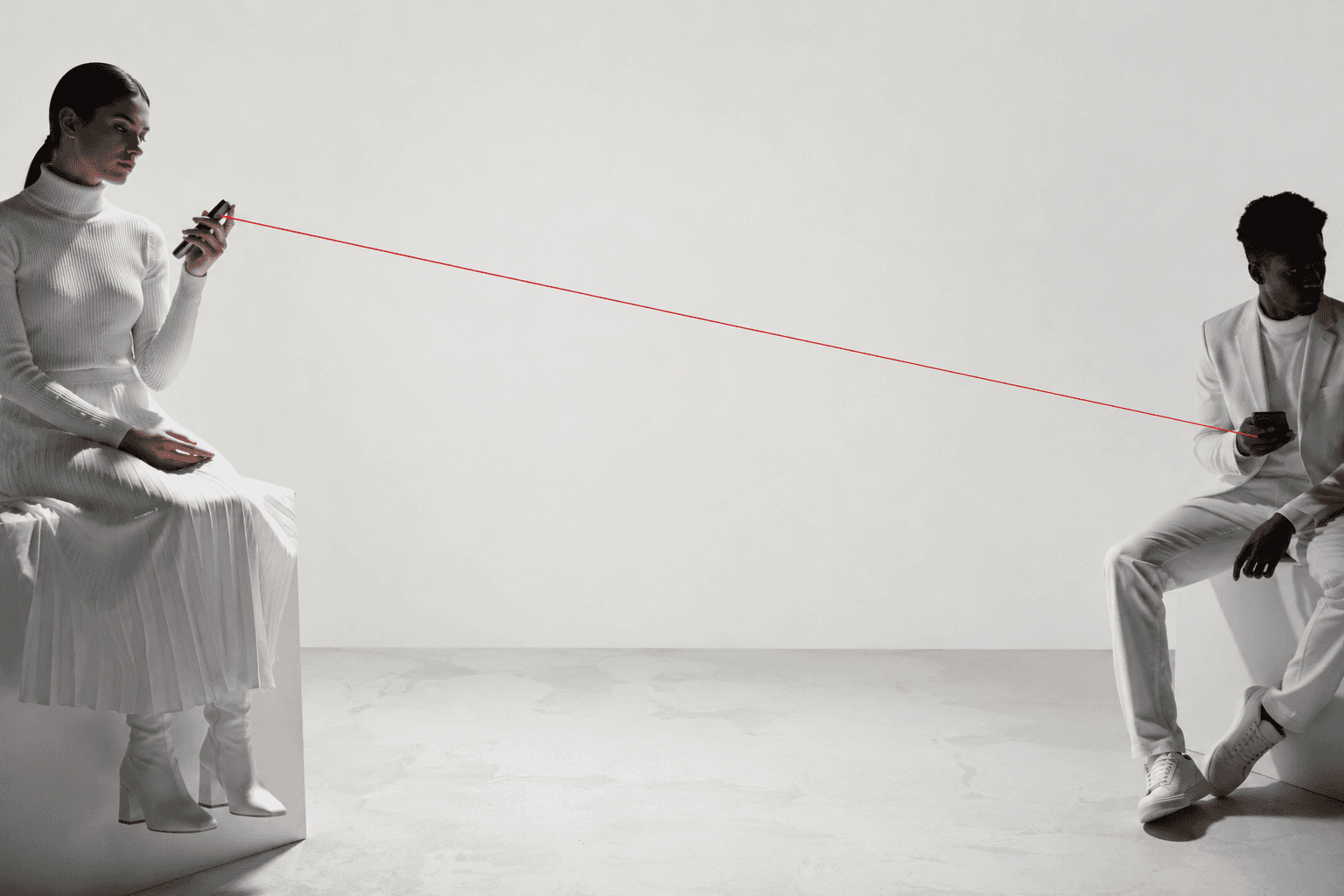 Two seated people connected by a thin red thread across an otherwise empty room.
